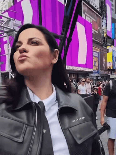 A Woman In A Black Leather Jacket Stands In Front Of A Chicago Sign GIF