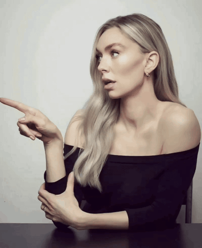A Woman In A Black Off The Shoulder Top Points Her Finger At Something GIF