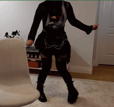 A Woman In A Black Outfit Is Standing In Front Of A White Chair GIF