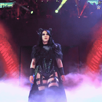 A Woman In A Black Outfit Stands On A Stage With A Sign That Says ' Wwe ' On It GIF