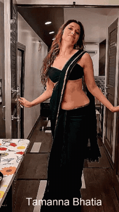 A Woman In A Black Saree Is Standing In A Hallway With The Name Tamanna Bhatia On The Bottom Right GIF
