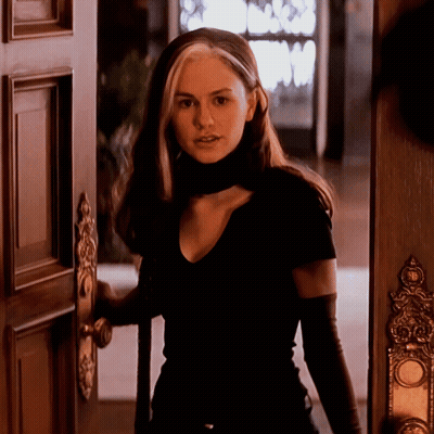 A Woman In A Black Shirt And Black Gloves Stands In A Doorway GIF