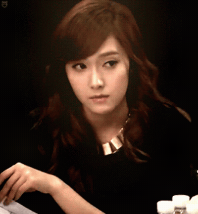 A Woman In A Black Shirt And Gold Necklace Looks At Something GIF