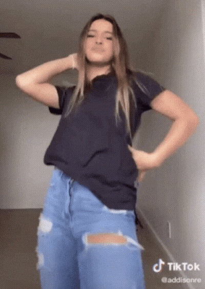A Woman In A Black Shirt And Ripped Jeans Is Dancing On A Tiktok GIF