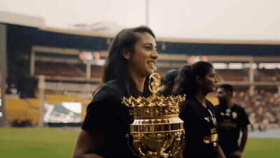 A Woman In A Black Shirt Holds A Gold Trophy With A Crown On It GIF