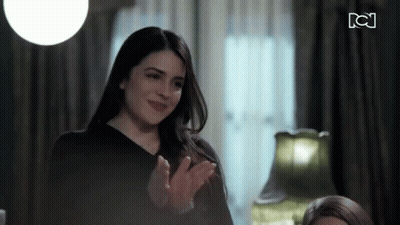 A Woman In A Black Shirt Is Clapping Her Hands In Front Of A Sign That Says Tc GIF