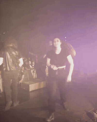 A Woman In A Black Shirt Is Dancing In Front Of A Crowd Of People GIF