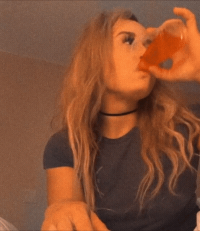A Woman In A Black Shirt Is Drinking From A Small Cup GIF