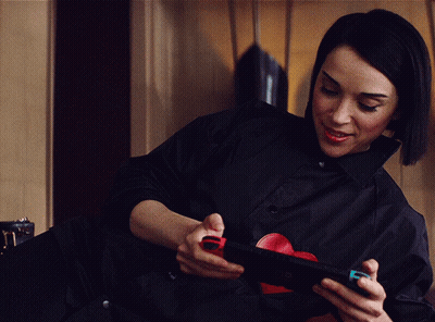 A Woman In A Black Shirt Is Holding A Nintendo Switch In Her Hands GIF