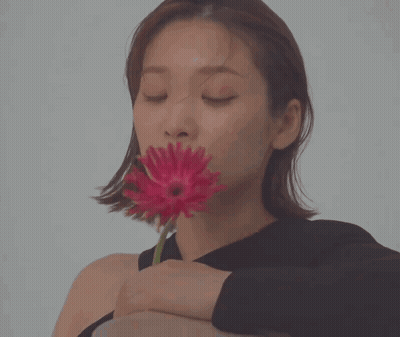 A Woman In A Black Shirt Is Holding A Red Flower In Her Hand GIF