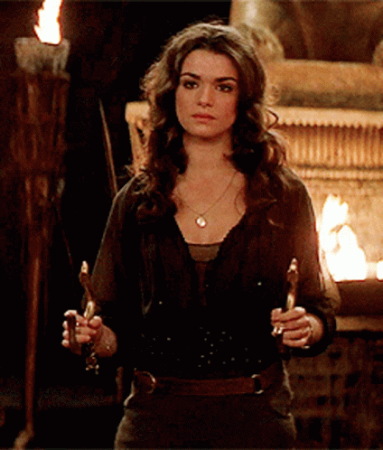 A Woman In A Black Shirt Is Holding Two Candles In Front Of A Fire GIF