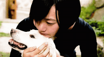 A Woman In A Black Shirt Is Kissing A White Dog On The Nose GIF