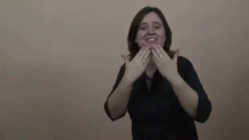 A Woman In A Black Shirt Is Making A Gesture With Her Hands And Smiling . GIF