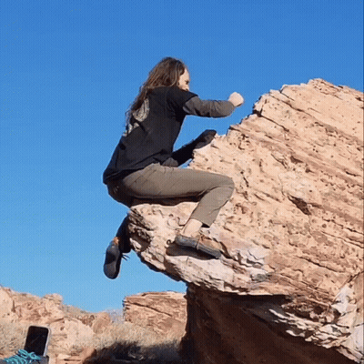 A Woman In A Black Shirt Is Sitting On A Large Rock GIF