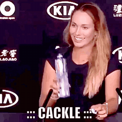 A Woman In A Black Shirt Is Smiling And Holding A Bottle With The Word Cackle Written On The Bottom GIF