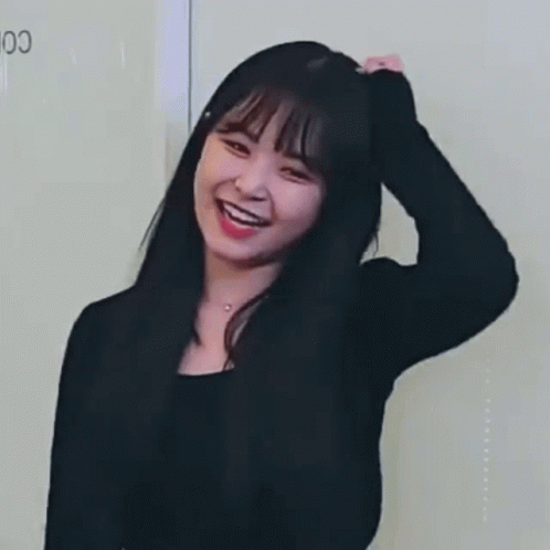 A Woman In A Black Shirt Is Smiling And Touching Her Hair . GIF