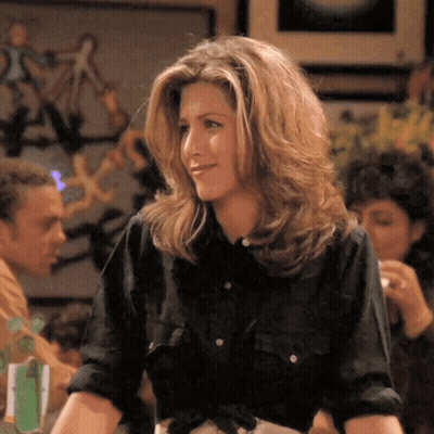 A Woman In A Black Shirt Is Smiling In A Room GIF