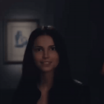 A Woman In A Black Shirt Is Smiling In Front Of A Framed Picture GIF