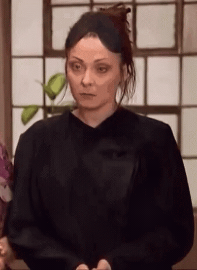 A Woman In A Black Shirt Is Standing In Front Of A Window And Looking At The Camera . GIF