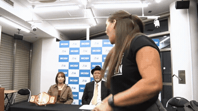A Woman In A Black Shirt That Says ' N ' On It Stands In Front Of A Blue And White Backdrop GIF