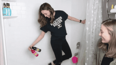 A Woman In A Black Shirt That Says Western Soccer Stands In A Shower GIF