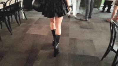 A Woman In A Black Skirt And Black Boots Is Walking On A Tile Floor GIF