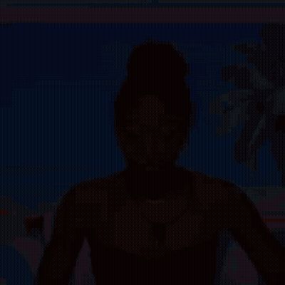A Woman In A Black Strapless Top And Necklace Is Sitting In Front Of A Beach Scene . GIF