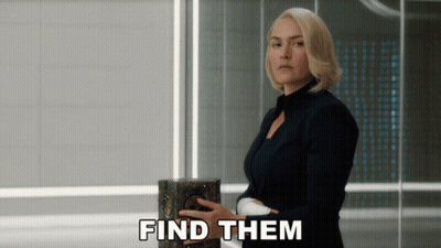 A Woman In A Black Suit Is Holding A Box With The Words Find Them Below Her GIF