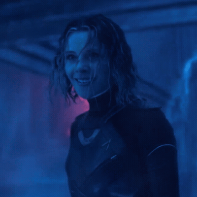 A Woman In A Black Suit Is Smiling In A Dark Room GIF