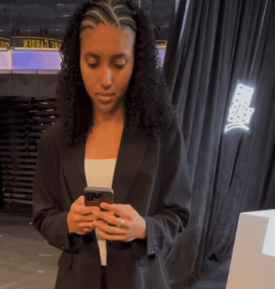 A Woman In A Black Suit Looks At Her Phone GIF