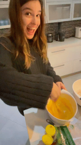 A Woman In A Black Sweater Is Mixing A Yellow Liquid In A White Bowl GIF