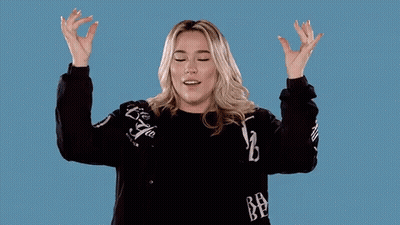 A Woman In A Black Sweater Is Raising Her Arms In The Air GIF