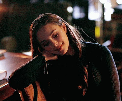 A Woman In A Black Sweater Is Sitting In A Chair With Her Head Resting On Her Hand . GIF