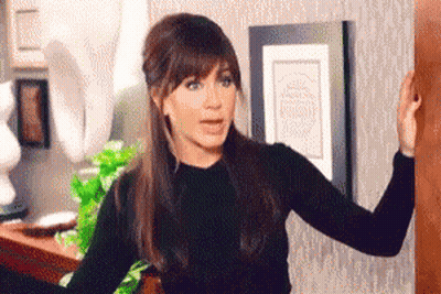 A Woman In A Black Sweater Is Standing Next To A Door . GIF