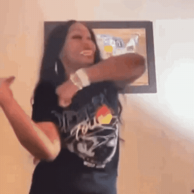 A Woman In A Black T-Shirt Is Dancing In A Room . GIF