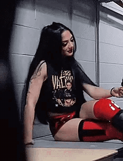 A Woman In A Black Tank Top And Red Shorts Is Sitting On A Bench . GIF