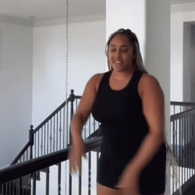 A Woman In A Black Tank Top And Shorts Is Dancing On A Staircase . GIF