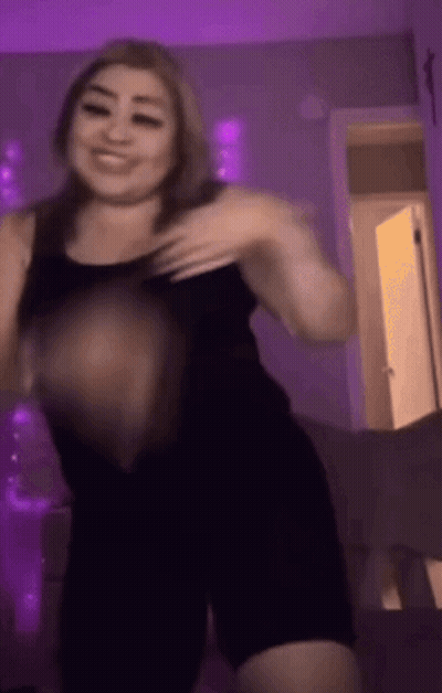 A Woman In A Black Tank Top Is Dancing In A Room With Purple Lights GIF