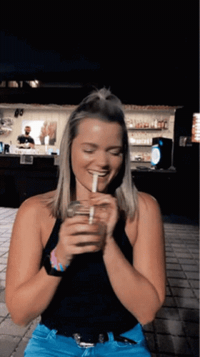 A Woman In A Black Tank Top Is Drinking From A Glass With A Straw GIF