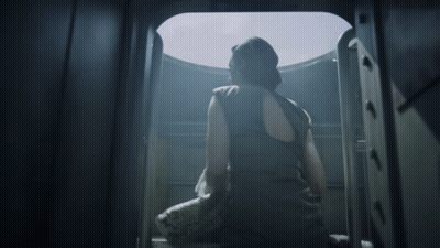 A Woman In A Black Tank Top Is Looking Out A Window GIF