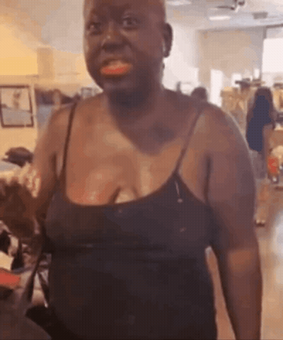 A Woman In A Black Tank Top Is Standing In A Living Room And Smiling . GIF
