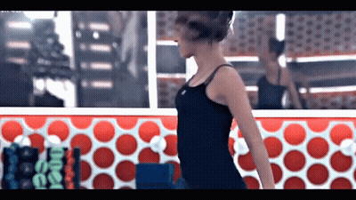 A Woman In A Black Tank Top Is Standing In Front Of A Red And White Polka Dot Wall .. GIF