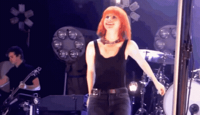 A Woman In A Black Tank Top Is Standing On Stage GIF