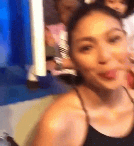 A Woman In A Black Tank Top Is Taking A Selfie With Her Tongue Out GIF
