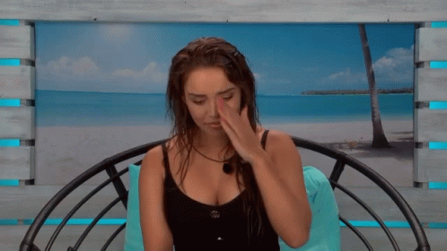 A Woman In A Black Tank Top Sits In A Chair With A Picture Of A Beach In The Background GIF