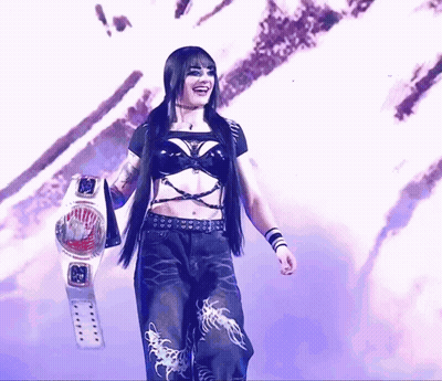 A Woman In A Black Top And Black Pants Holds A Wrestling Belt GIF