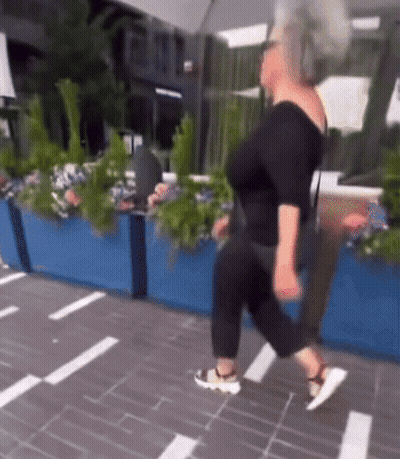 A Woman In A Black Top And Black Pants Is Walking Down The Street GIF