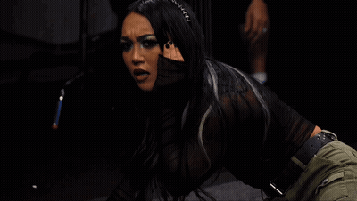 A Woman In A Black Top And Green Pants Is Kneeling Down In A Dark Room GIF