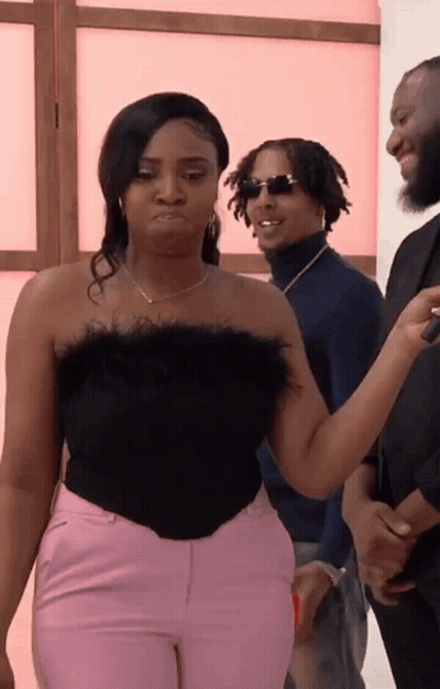 A Woman In A Black Top And Pink Pants Is Standing Next To A Man In A Blue Sweater . GIF
