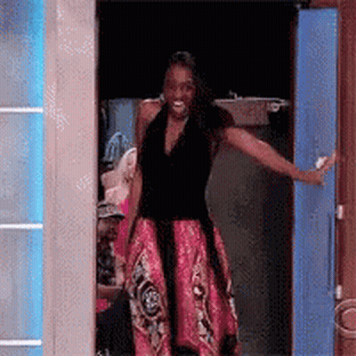 A Woman In A Black Top And Pink Skirt Is Standing In A Doorway With Her Arms Outstretched . GIF